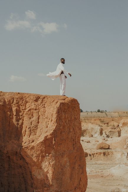 A man in a white outfit stands on a cliff edge in Lagos, capturing a desert-like landscape.