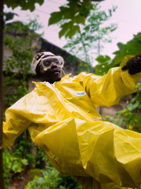 Man outdoors wearing yellow protective suit and goggles amidst greenery, showing safety measures in a garden environment.