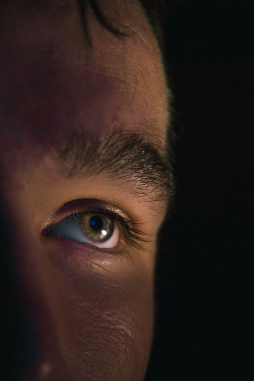 Free Intimate close-up of a man's eye lit against a dark background, capturing detail and emotion. Stock Photo