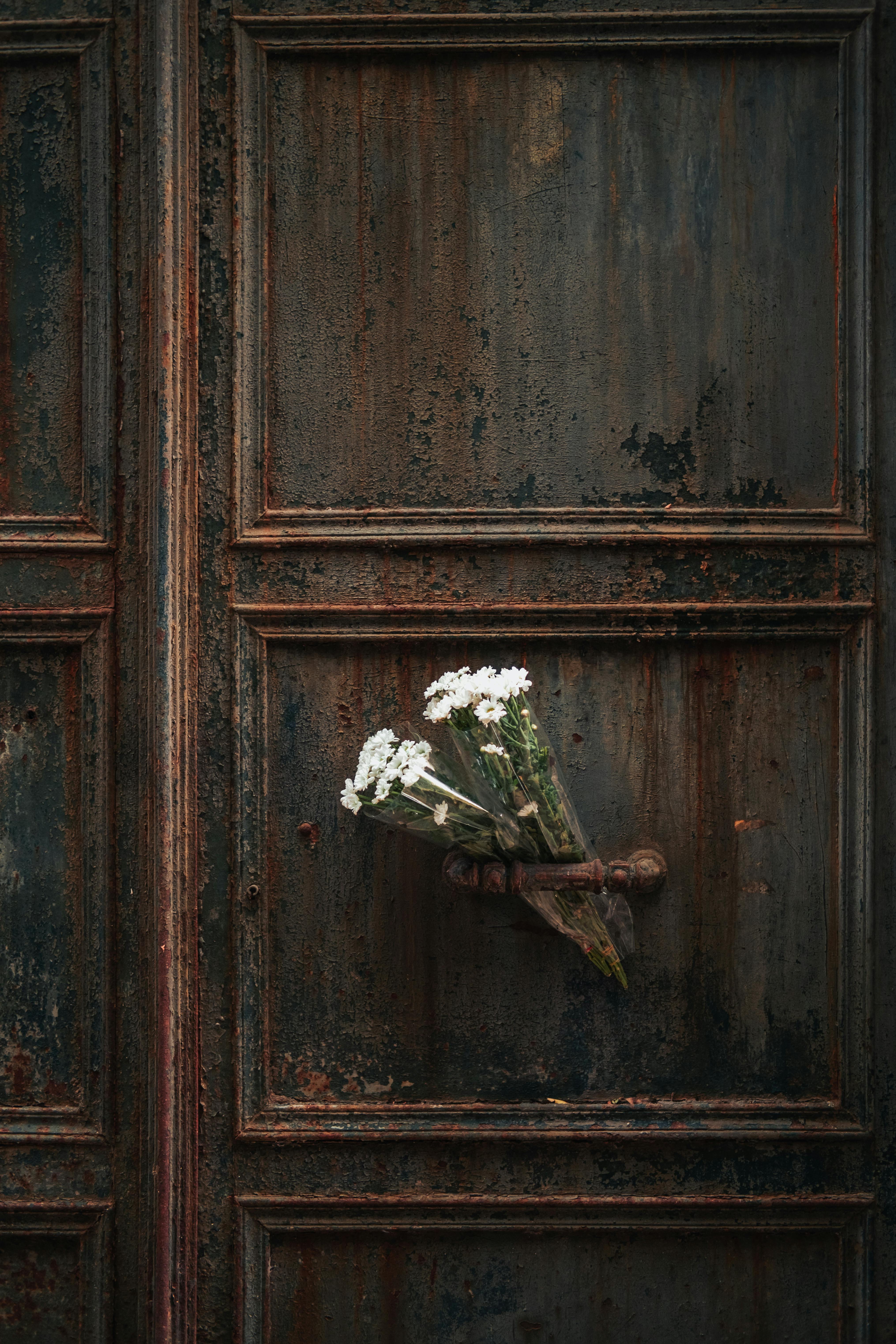 A rustic old door with a small bouquet of white flowers tucked in the handle.