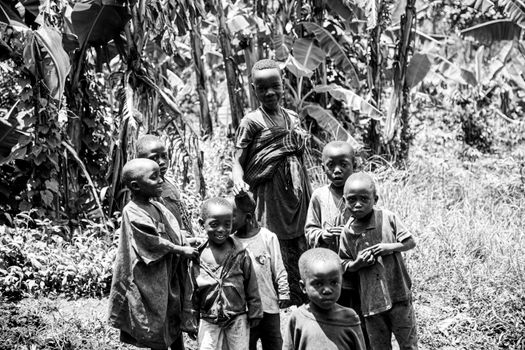 Group of children smiling outdoors in black and white, surrounded by lush plants.