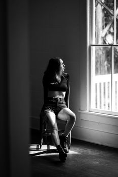 Black and white photo of a woman sitting on a chair by a window, exuding a contemplative mood.