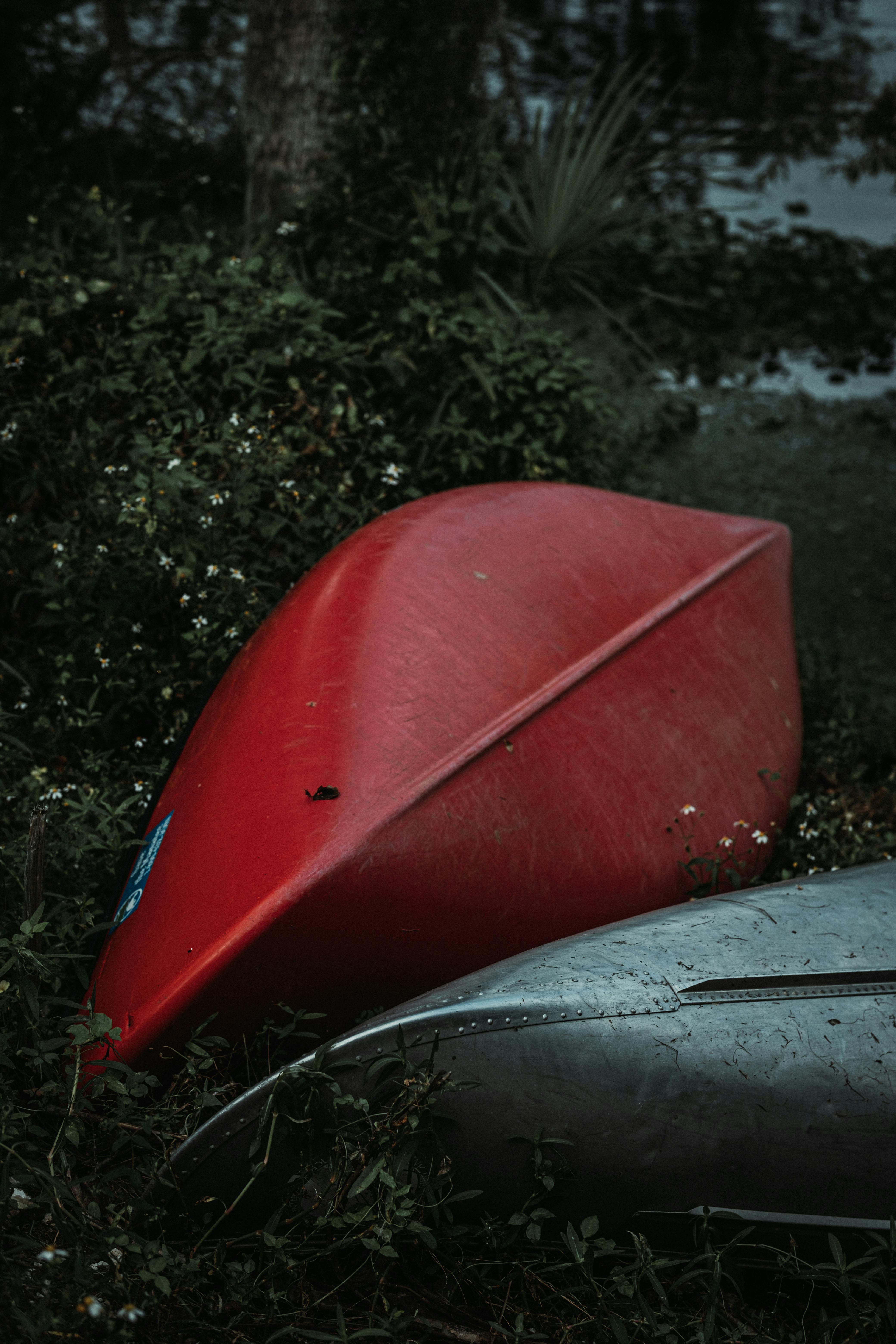 A red and silver canoe abandoned by the lake, surrounded by lush greenery.
