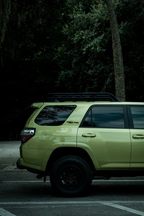 Free A green SUV parked outdoors near a forested area. Captures half the vehicle with trees in the background. Stock Photo