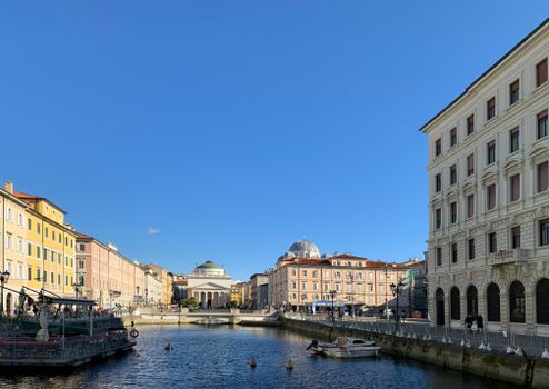 Beautiful view of the canal and historic buildings in Trieste, Italy under a clear blue sky.