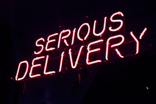 Bright pink neon sign displaying 'SERIOUS DELIVERY' at night, perfect for urban aesthetics.