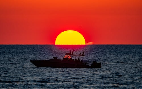 Silhouetted Boat on a Sea against a Large Setting Sun 