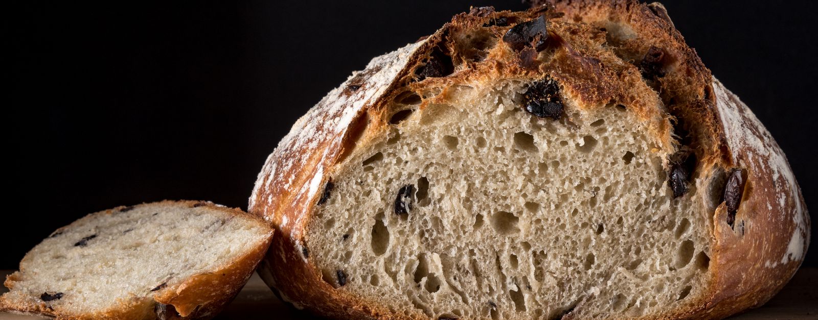 Delicious artisan olive bread loaf with one slice on wooden board, perfect for healthy eating.