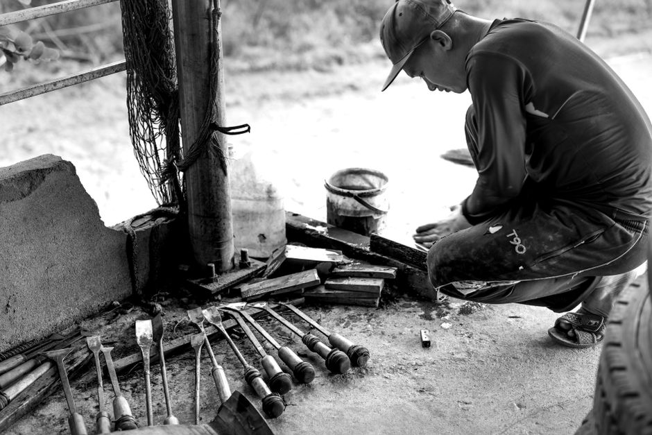 Black and white image of a craftsman working with tools outdoors.
