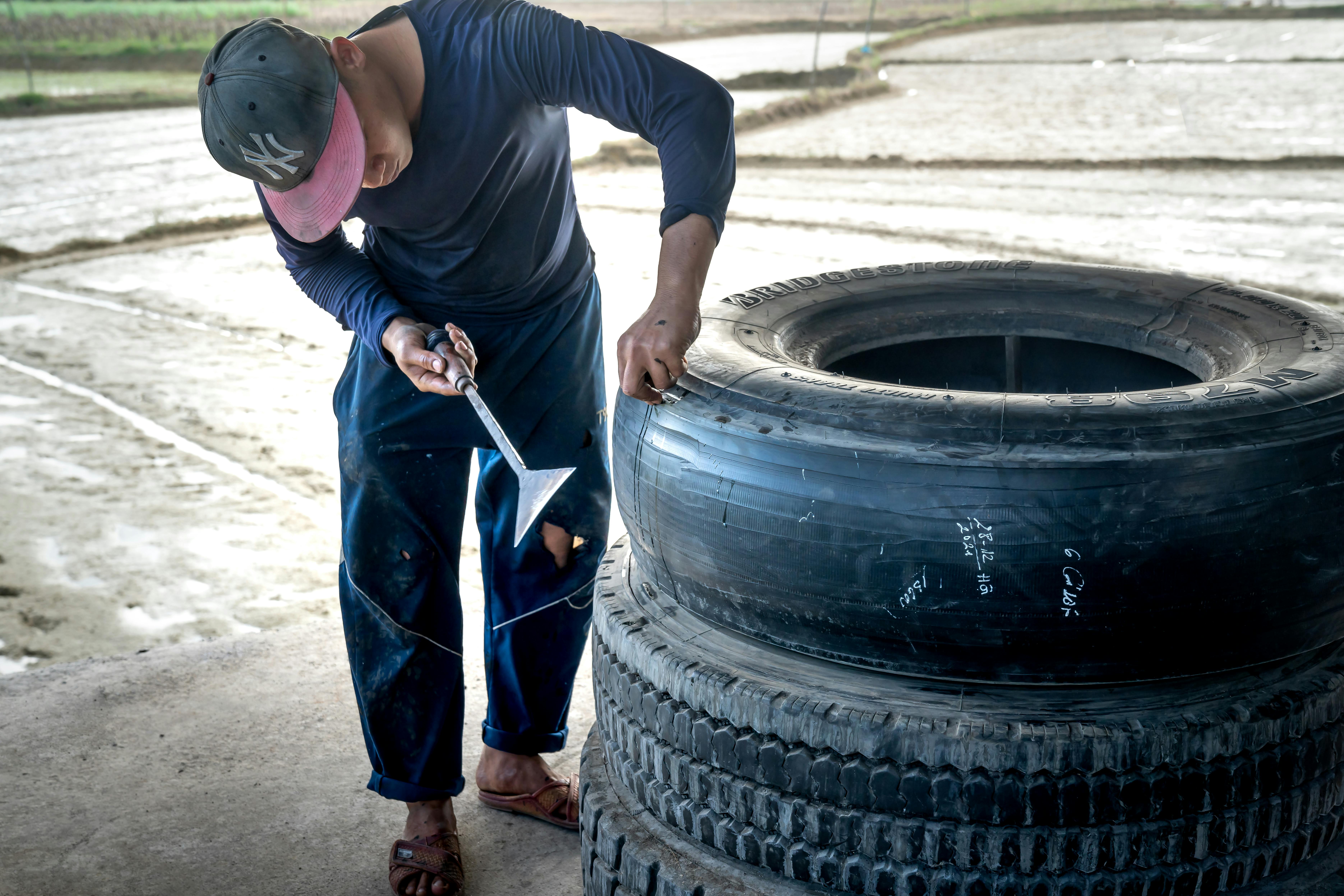 Extend tire life Tire rotation Vehicle maintenance A man works on a large tire outdoors, using a tool for repairs.