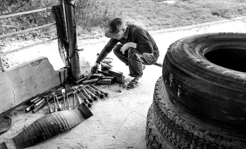 Free Black and white photo of a crouching worker with tools and tires in an outdoor setting. Stock Photo