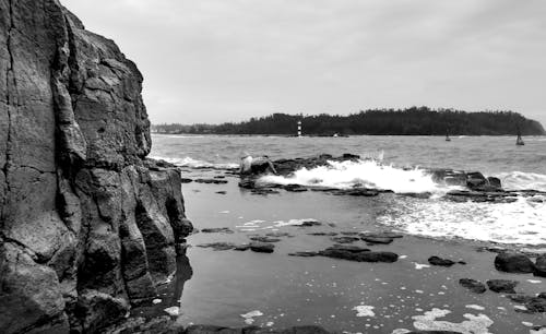 People on Sea Shore with Rock and Stones in Black and White under Clouds