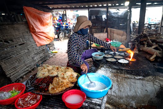 A woman prepares traditional food on a stone stove in an outdoor market setting.
