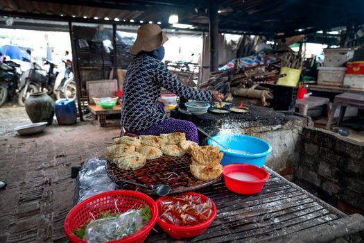 A woman prepares traditional food at a rustic outdoor market stall. Baking and selling.