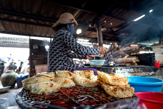 Street vendor cooking traditional pancakes at an outdoor market stall with colorful trays.