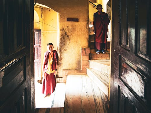 Man in Red Robe Standing near Brown Wooden Door