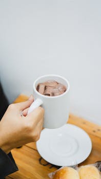 Close-up of a hand holding a mug of iced coffee indoors at a café in Madiun, Indonesia.
