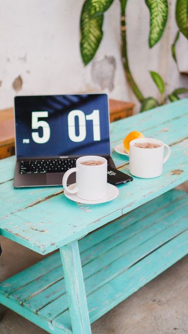 A tranquil workspace setup with coffee mugs and a laptop on a rustic teal table, perfect for remote work or relaxation.