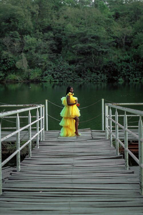 Woman in Yellow Dress Standing on Brown Wooden Dock