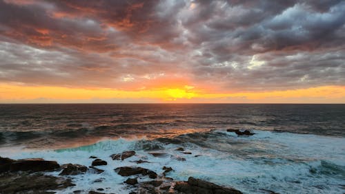 Rocky Shore Under Cloudy Sky during Sunset