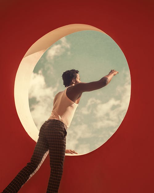 Man Looking Through a Round Window and Reaching His Hand 