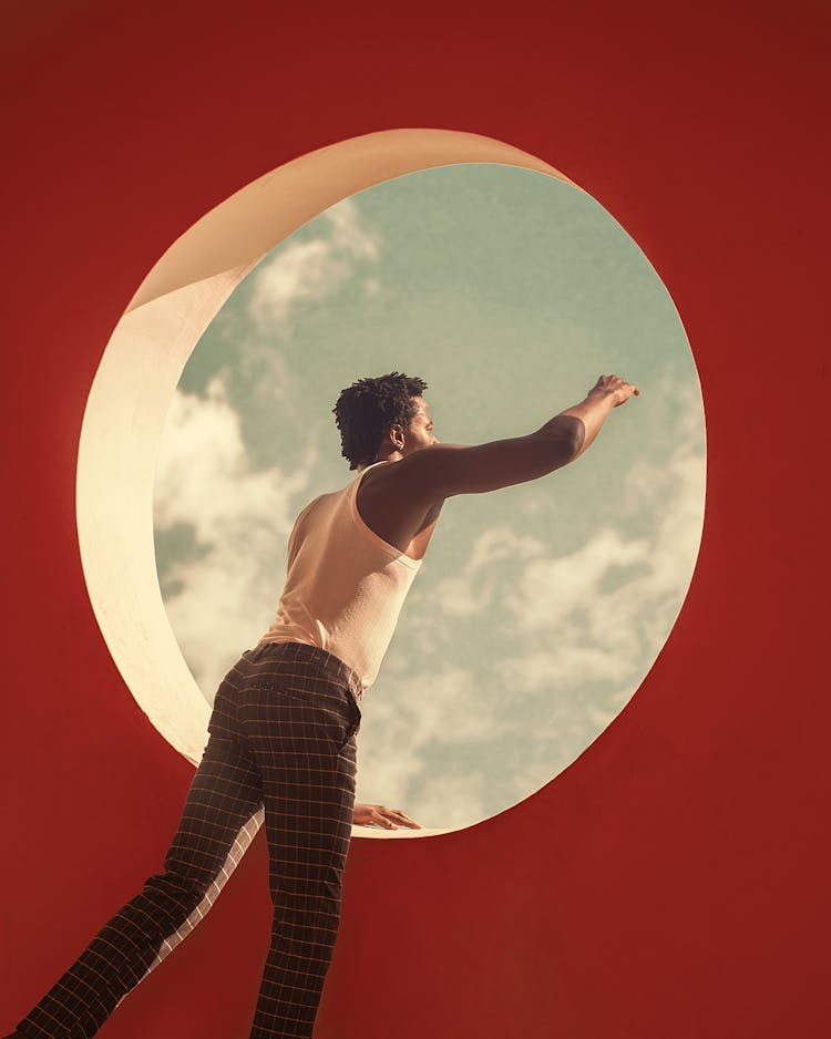 Man Looking Through A Round Window And Reaching His Hand 