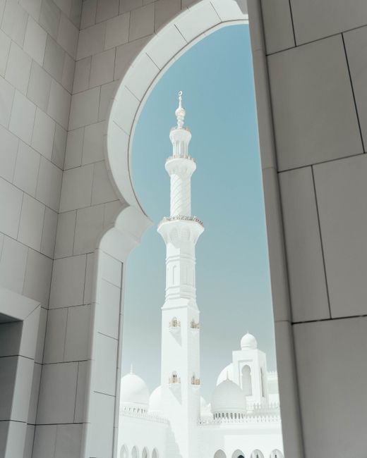 A beautiful mosque with a striking minaret viewed through a decorative arch, under a clear sky.