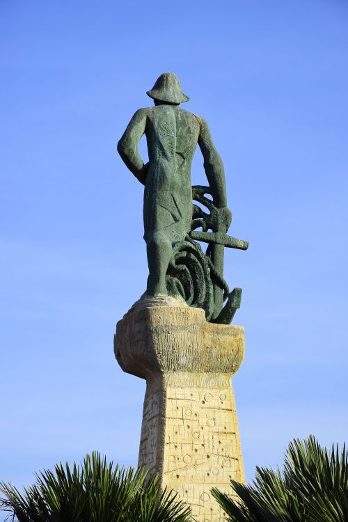 Free Bronze statue standing tall on a pedestal with clear blue sky background. Stock Photo
