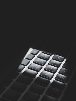 A moody close-up of a computer keyboard with dramatic lighting creating shadows.