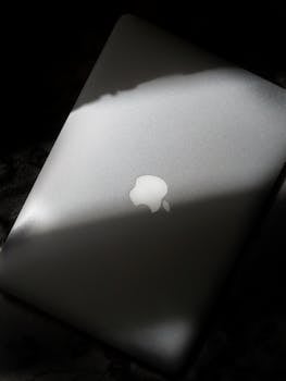 A sleek silver laptop with a glowing logo, partially illuminated by sunlight.