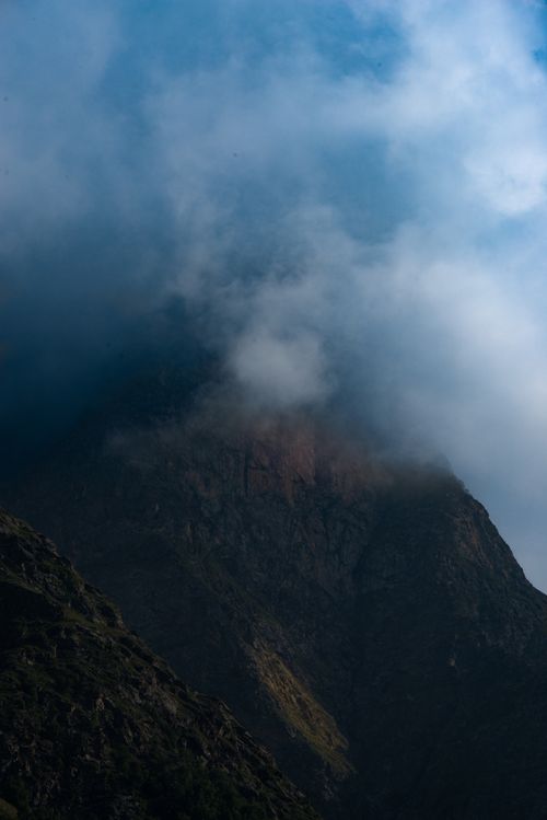 Free A dramatic mountain peak shrouded in fog and clouds under a blue sky. Stock Photo