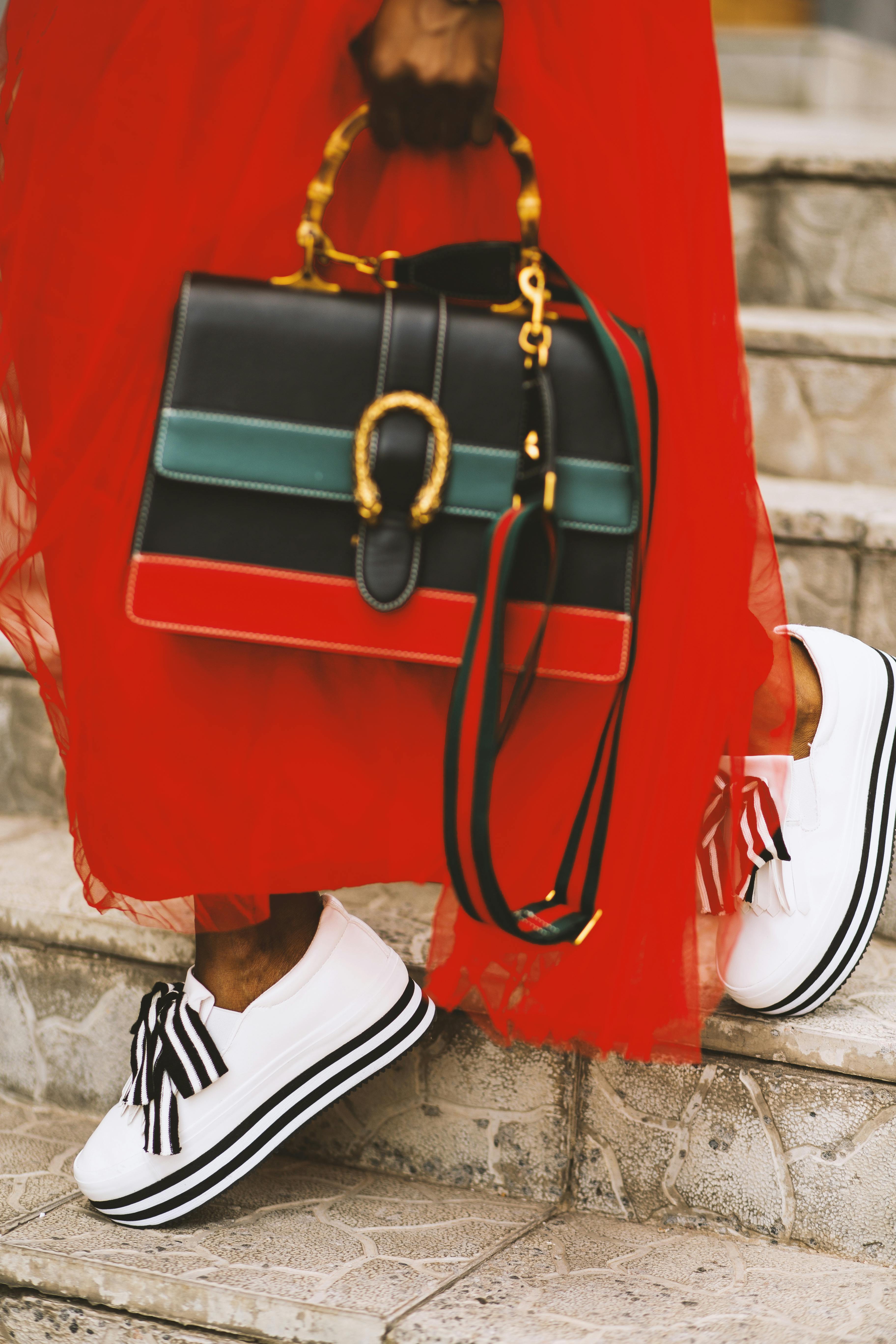 一个穿着红色连衣裙、时尚包和鞋子的女人站在楼梯上