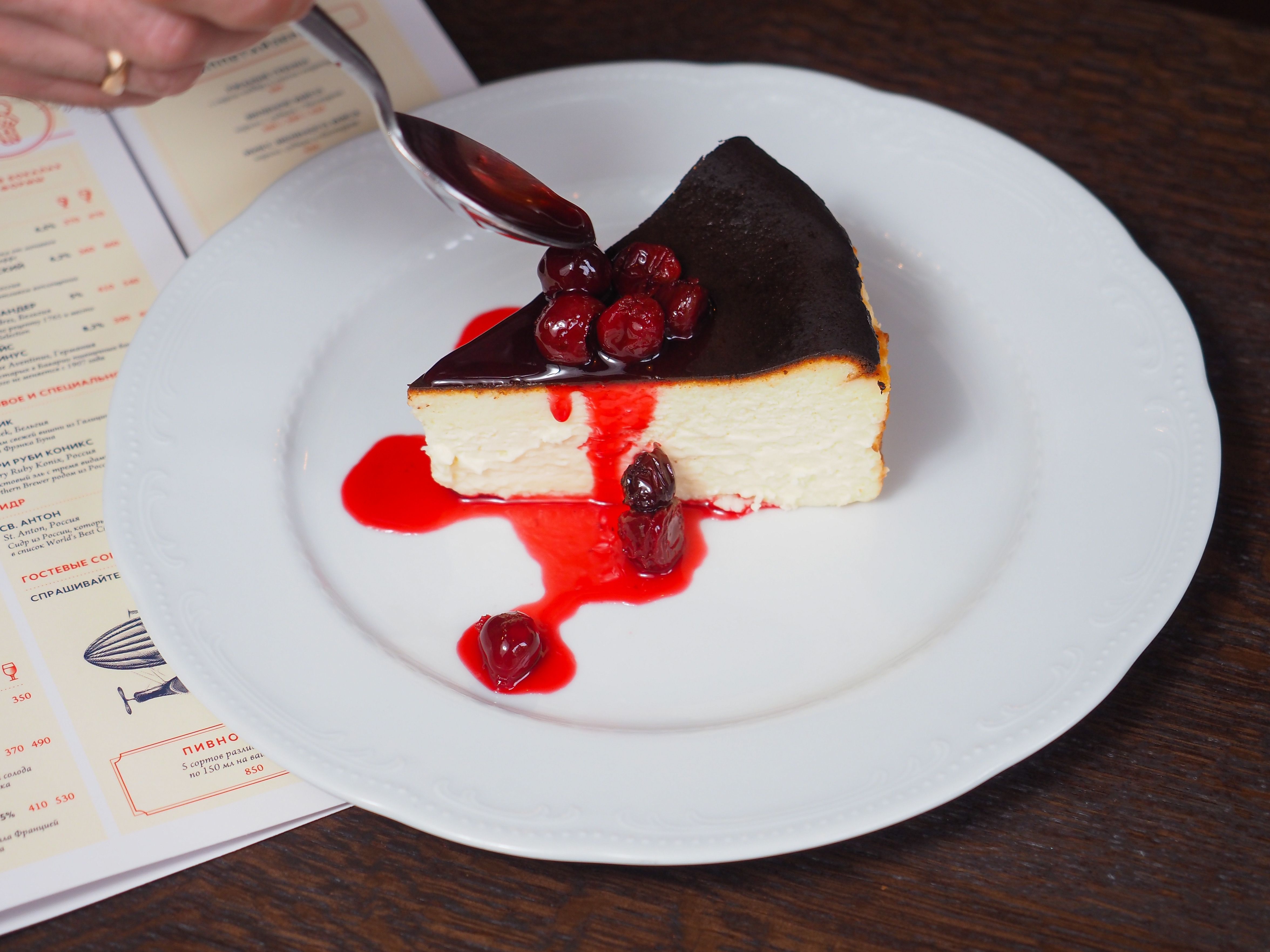 Close-up of a cheesecake slice with cherry sauce on a white plate, perfect dessert choice.