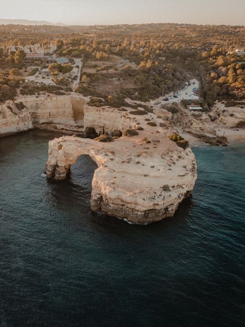 Stunning aerial shot of a natural rock arch along the Algarve coast, Portugal, at sunset.