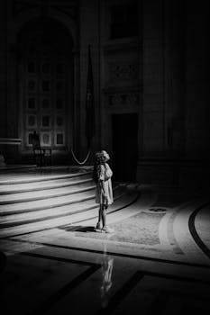 Black and white photo of a solitary woman standing in a cathedral, illuminated by sunlight.