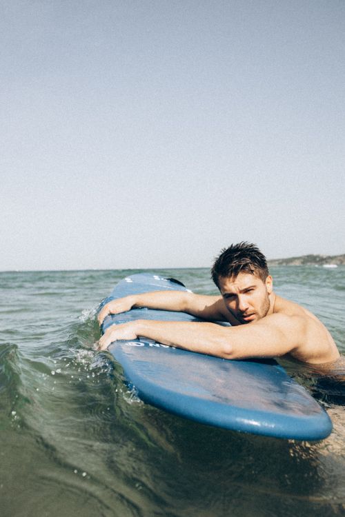 Free A young man relaxing on a blue surfboard in the ocean on a sunny day. Stock Photo