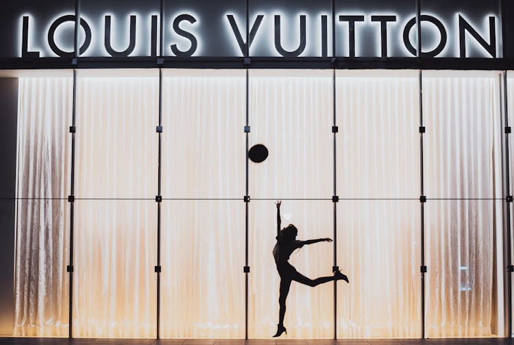 A Woman Jumping Beside Glass Wall With Louis Vuitton Signage
