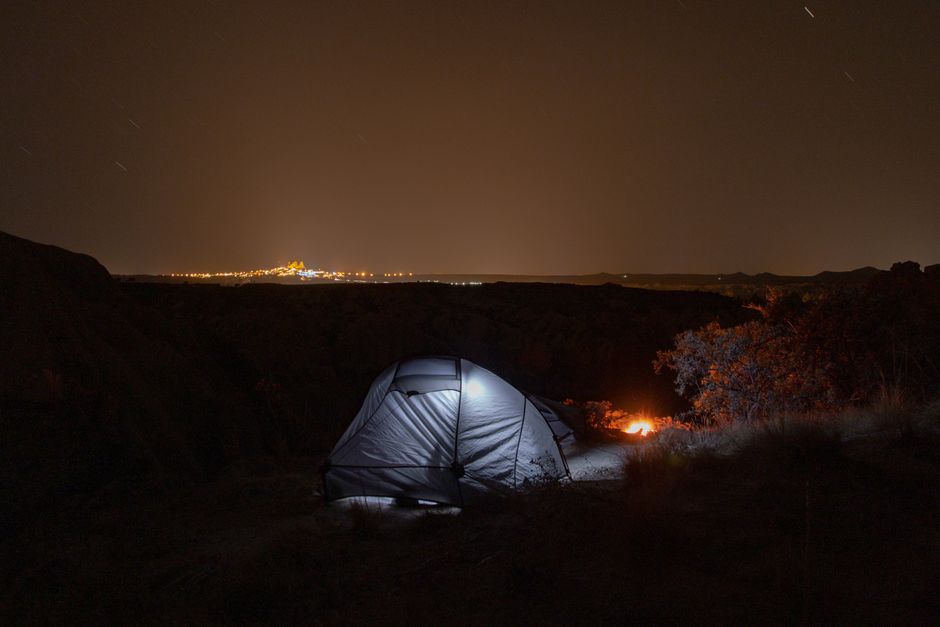Fotomural Escena de camping serena bajo un cielo estrellado con luces de la ciudad en el horizonte.