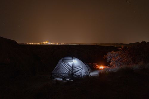 Free Serene camping scene under a starlit sky with city lights on the horizon. Stock Photo