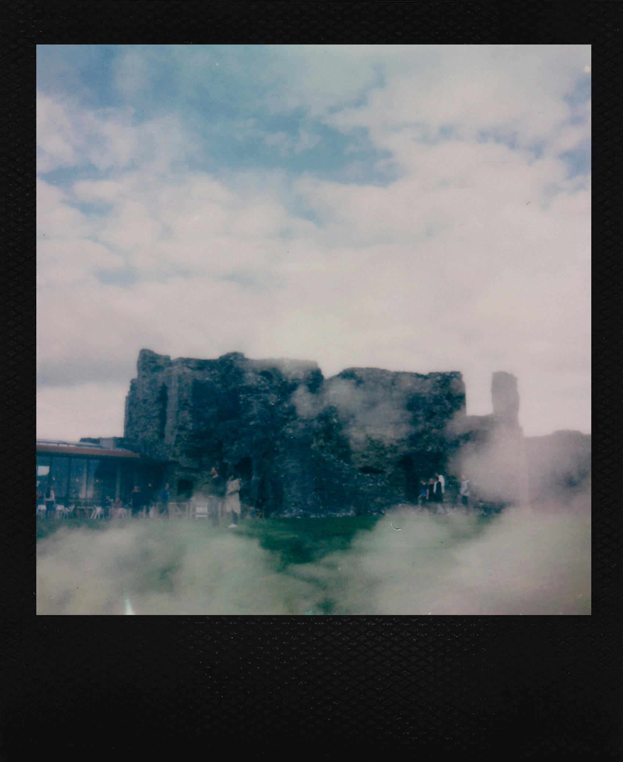 Historic ruins surrounded by fog and clouds in Denbigh, Wales, captured on polaroid.