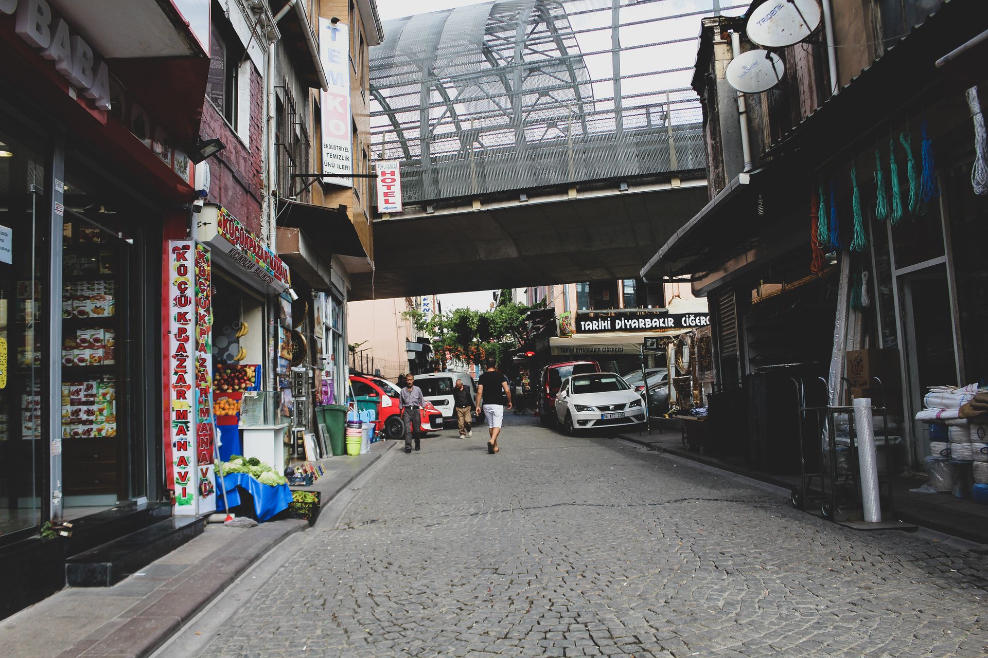 Urban street scene in Kocasinan, Kayseri, Turkey, with shops and pedestrians on a cobblestone road.