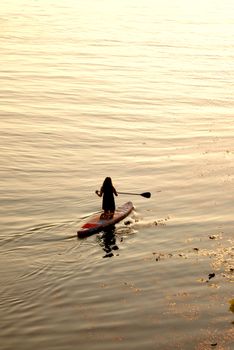 A woman enjoys paddleboarding during sunset on serene waters, providing a sense of tranquility and adventure.