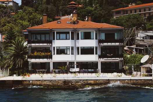 Elegant waterfront villa with red roofs in Kayseri, Turkey surrounded by lush greenery.