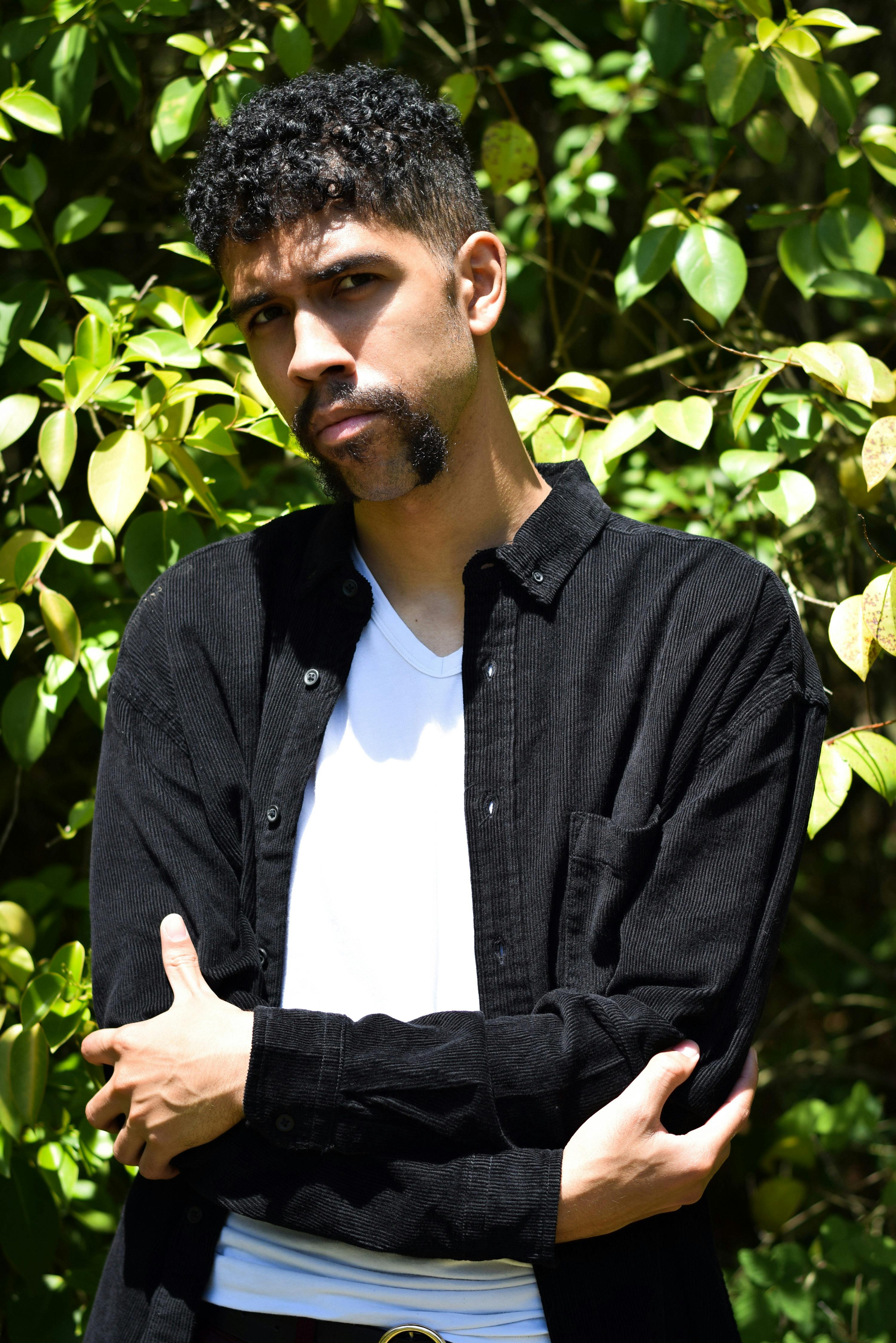 A Man in Black Denim Jacket Standing Near Green Plants while Posing at