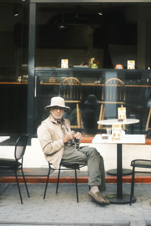 Free Senior man sitting outdoors at a cafe, enjoying a relaxed moment with a drink. Stock Photo
