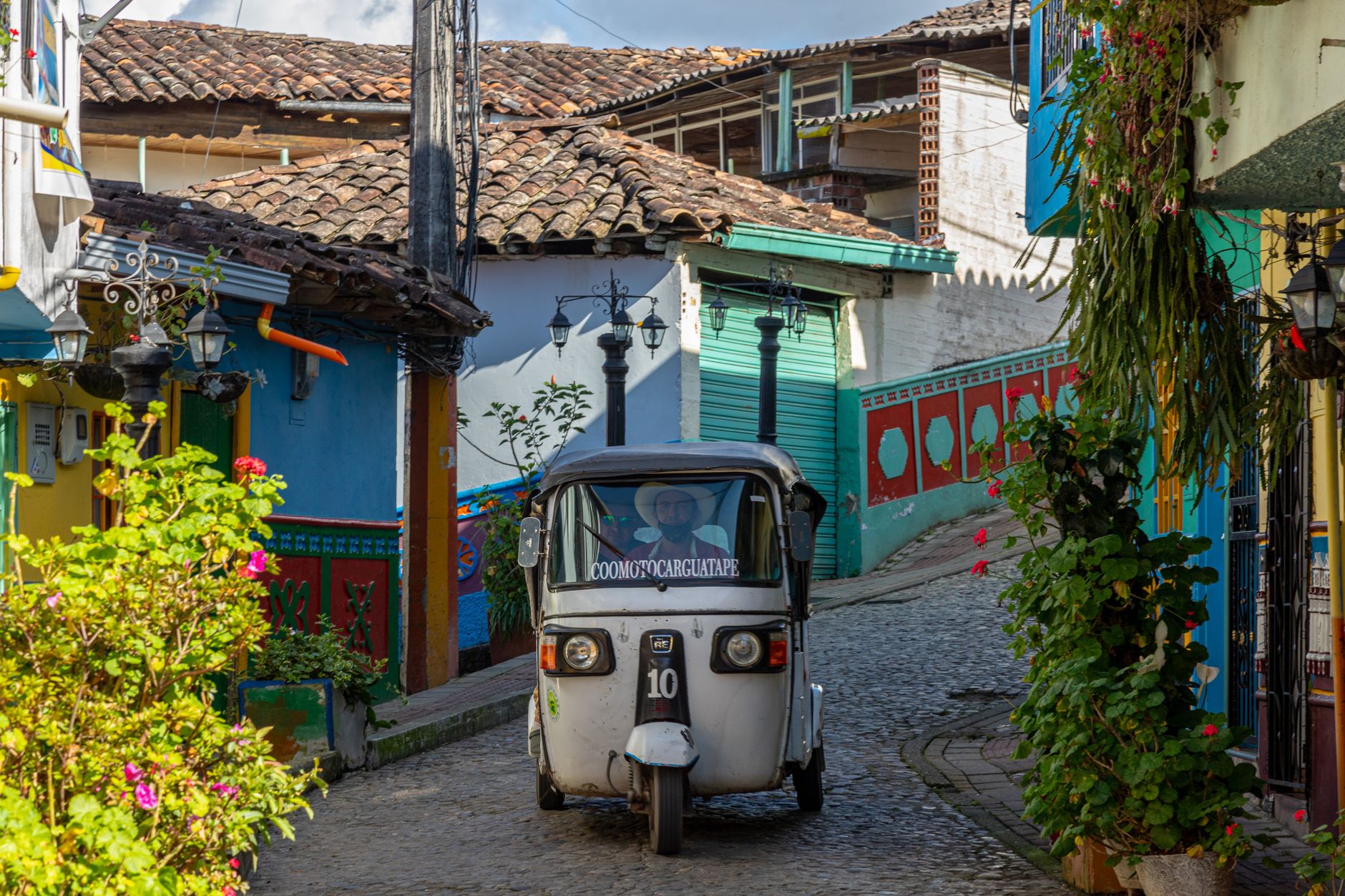 A vibrant tuk-tuk navigating the colorful, cobbled streets of Guatapé, Colombia.