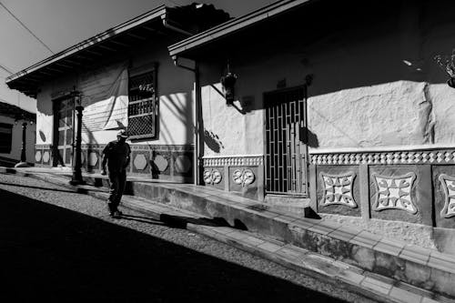 Grayscale Photo of a Man Walking on the Sidewalk