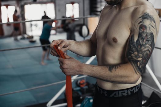 Tattooed boxer wrapping hands with tape in an indoor gym, showcasing fitness and dedication.