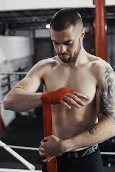 Caucasian man wrapping hands with red bandage in boxing gym. Focused on preparation.