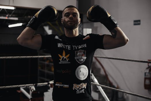 Boxer in gym with gloves flexing muscles, showcasing confidence and strength.